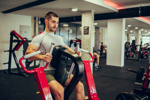 A strong fir sportsman is sitting at the chest pull machine at the